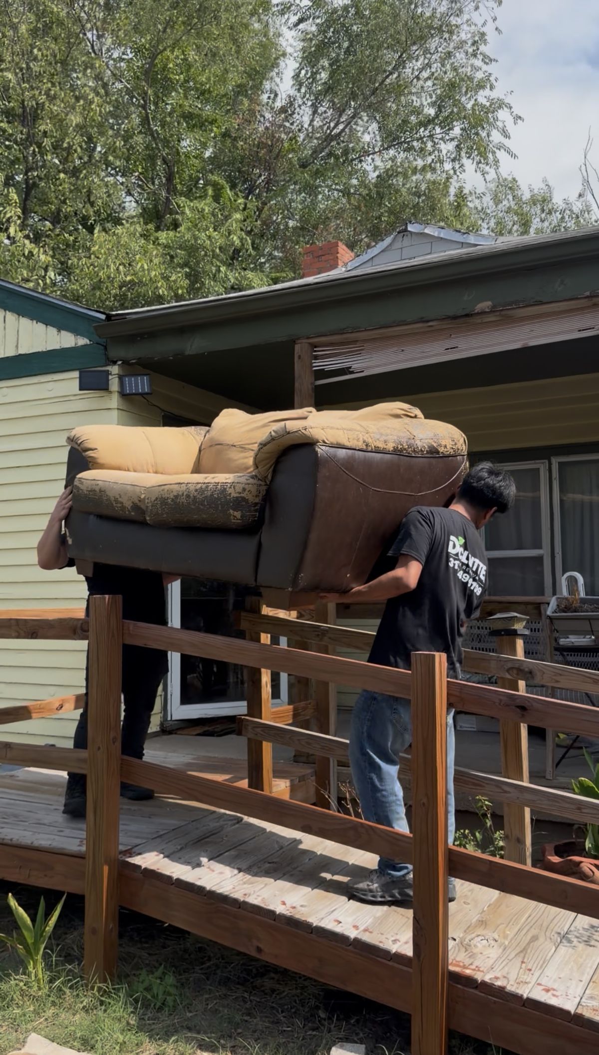 Two Declutter crew members carrying an old couch down a wooden ramp